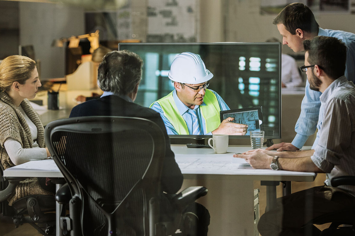 Construction manager discusses accounting with professionals in a virtual meeting, reviewing project details on a tablet.