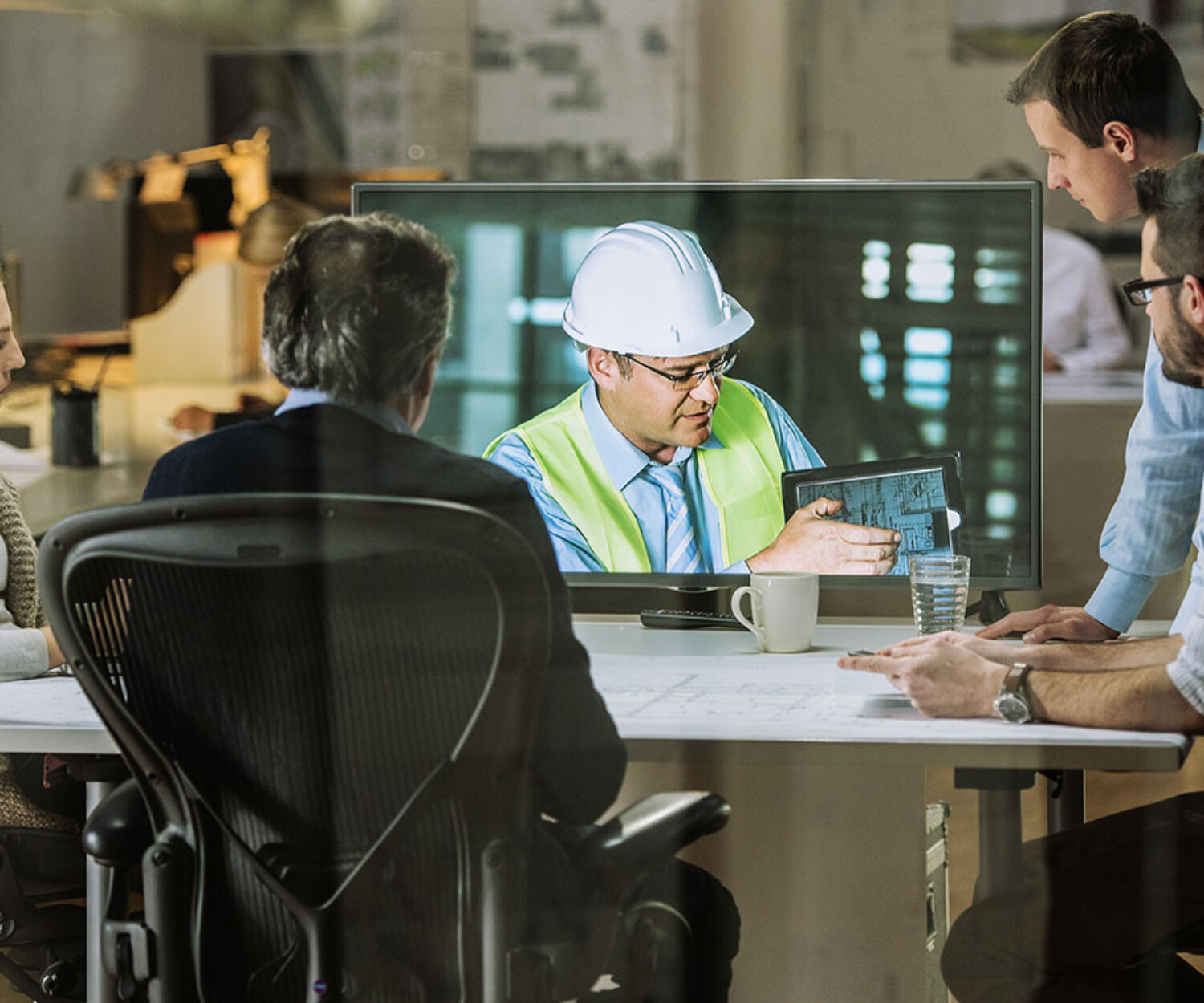 Construction manager discusses accounting with professionals in a virtual meeting, reviewing project details on a tablet.