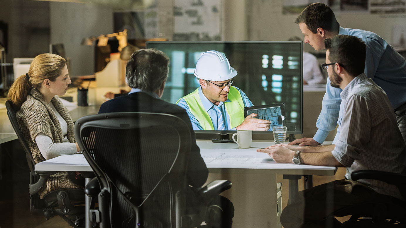 Construction manager discusses accounting with professionals in a virtual meeting, reviewing project details on a tablet.