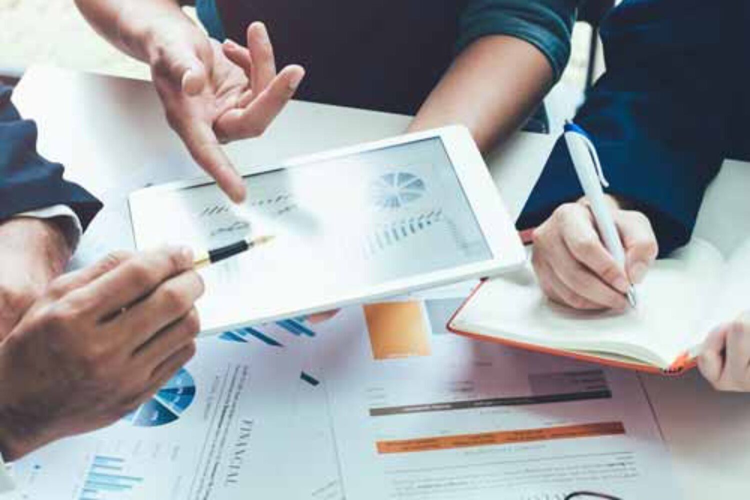 people looking at an iPad with a chart on it with someone taking notes