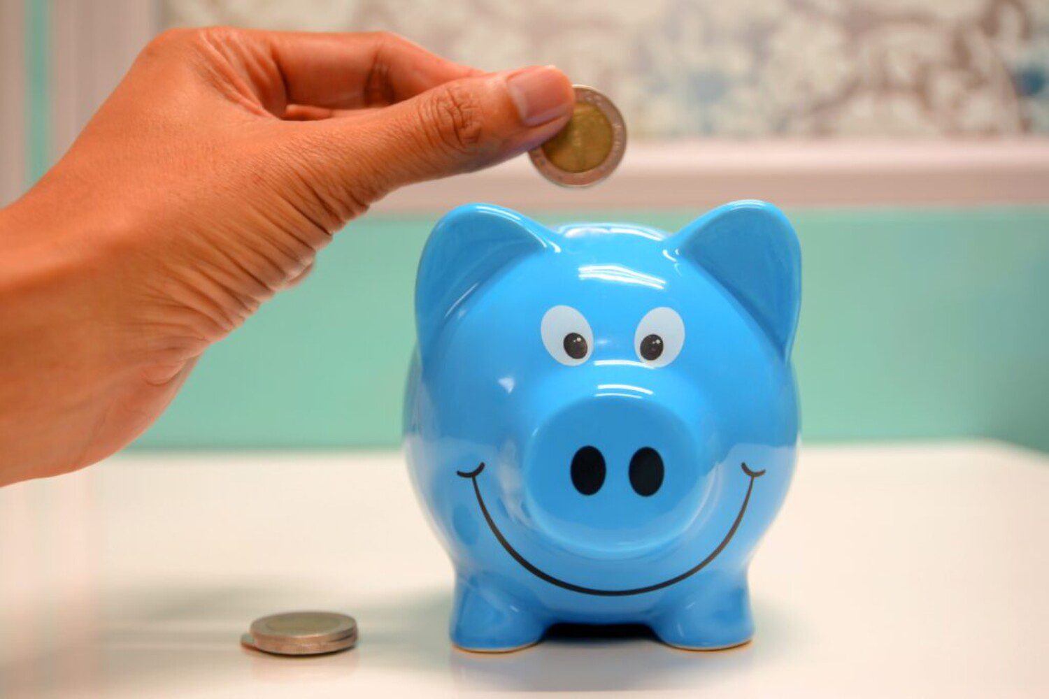 a hand putting in money into a blue piggy bank