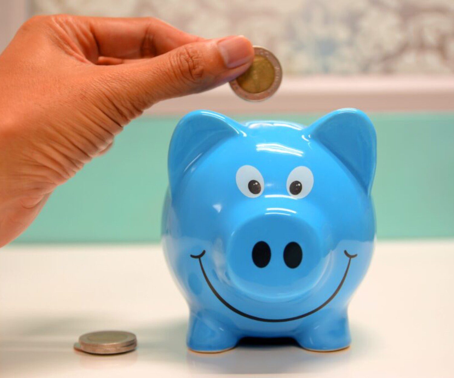 a hand putting in money into a blue piggy bank