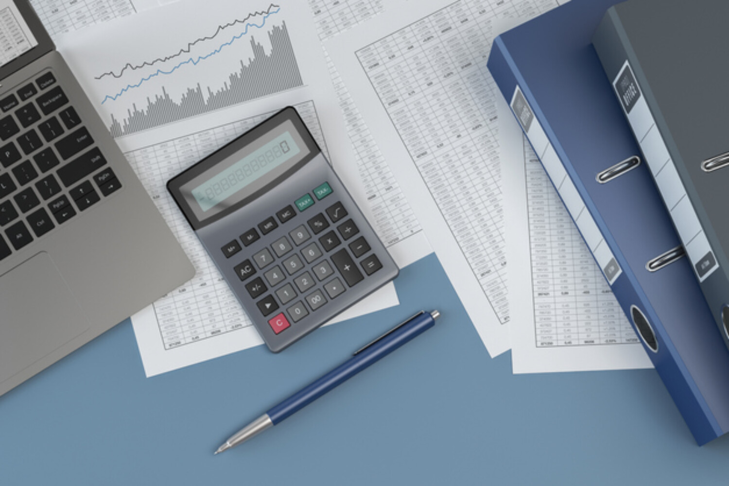 Office workspace with a laptop, calculator, financial documents with charts and tables, blue folders, and a pen on a blue desk.