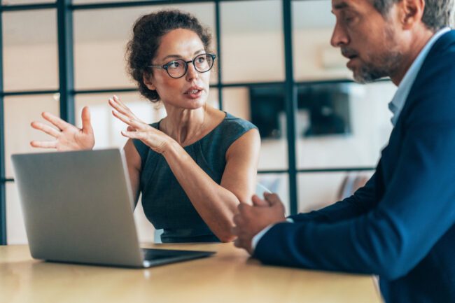 Two business people having a meeting and discussing new agreement. Working process in the office, businessman and business woman working together using laptop. Couple of business persons talking, they are engaged in a focused conversation